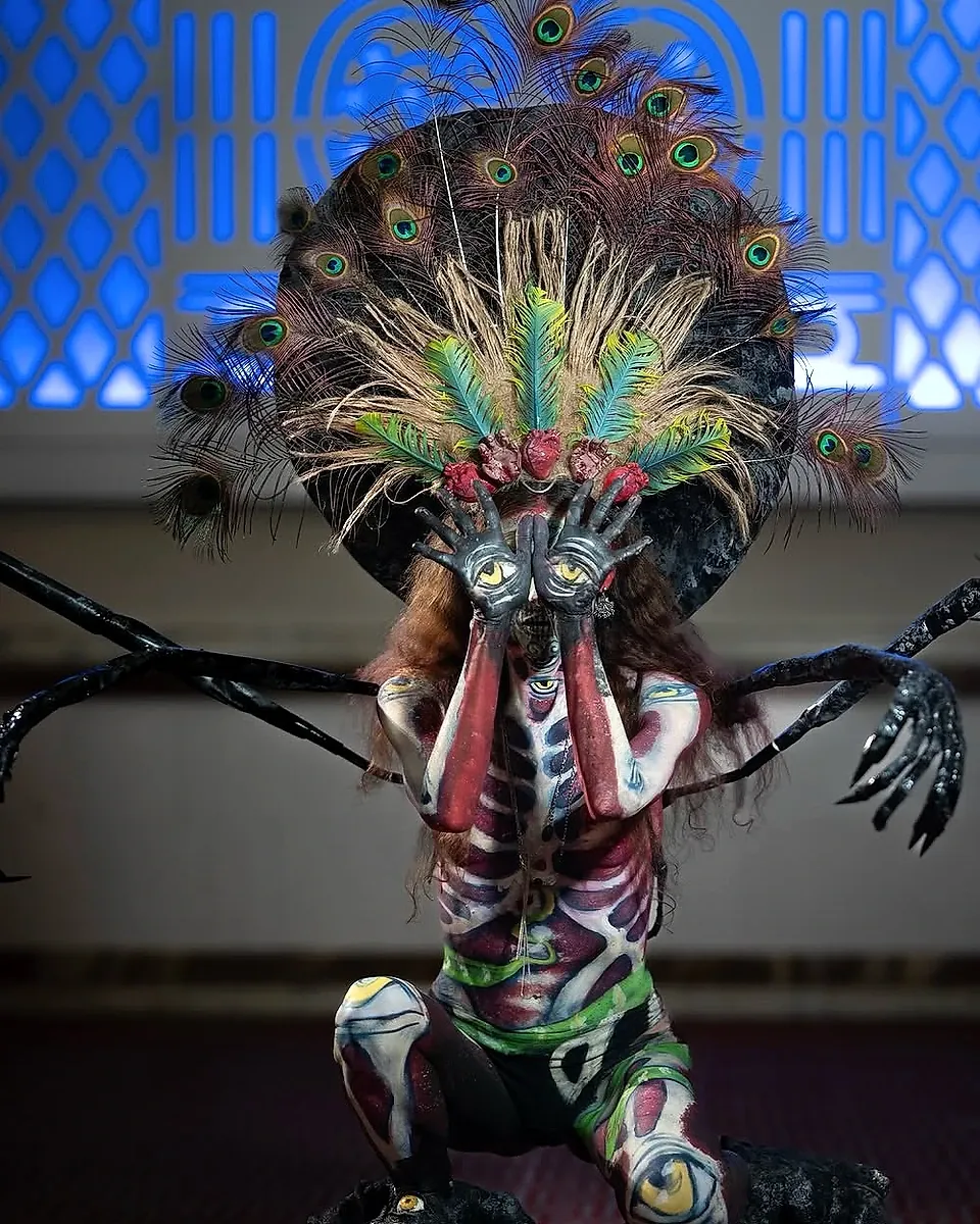 Caracterización de Catrina con ojos pintados en las manos y penacho de plumas en Guerra de Catrinas 2026