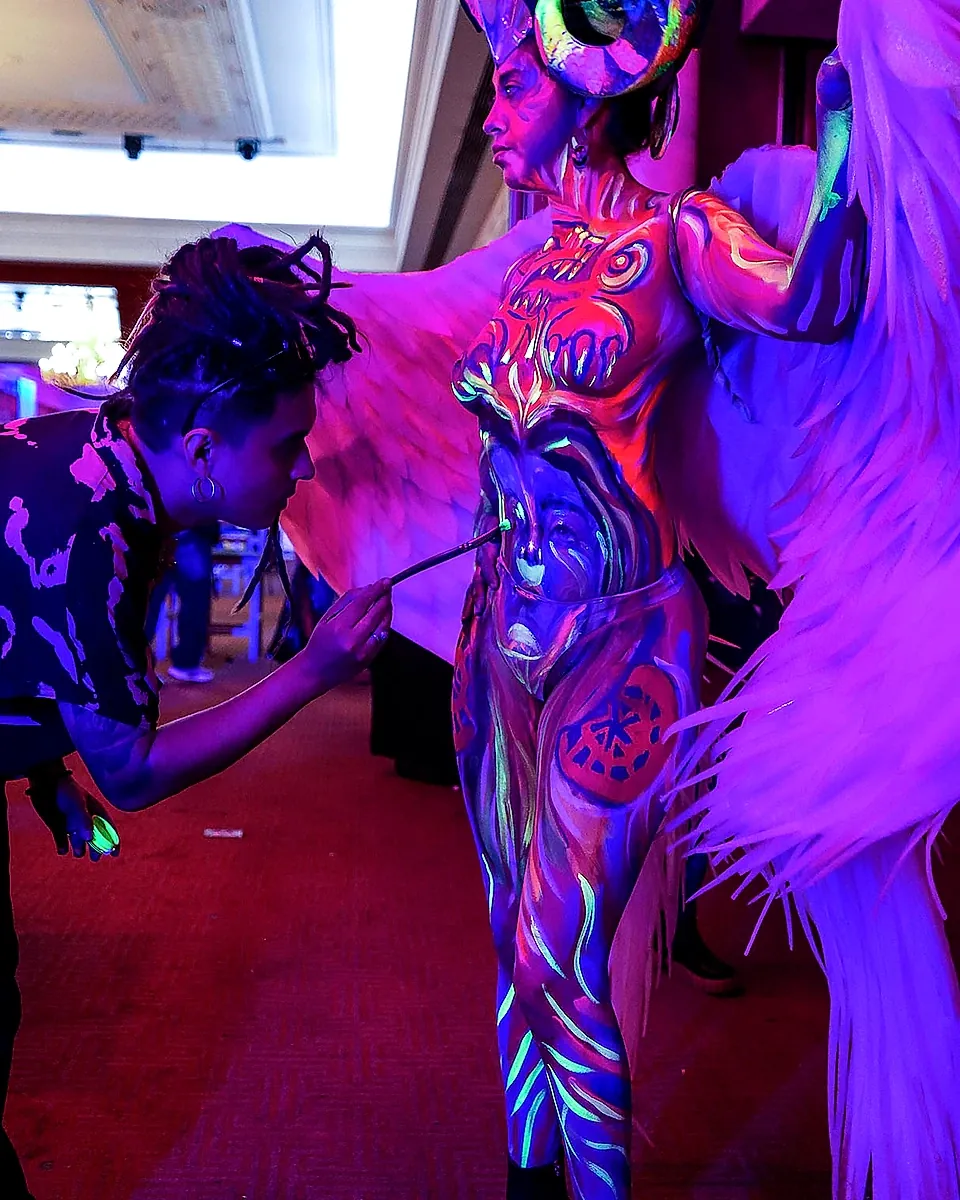 Maquillista pintando con pincel a modelo con bodypaint fluorescente UV durante Guerra de Catrinas 2026